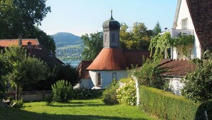 Un bâtiment traditionnel doté d’une tour imposante et d’un toit recouvert de tuiles rouges, entouré d’une végétation luxuriante et offrant une vue dégagée sur une vallée.