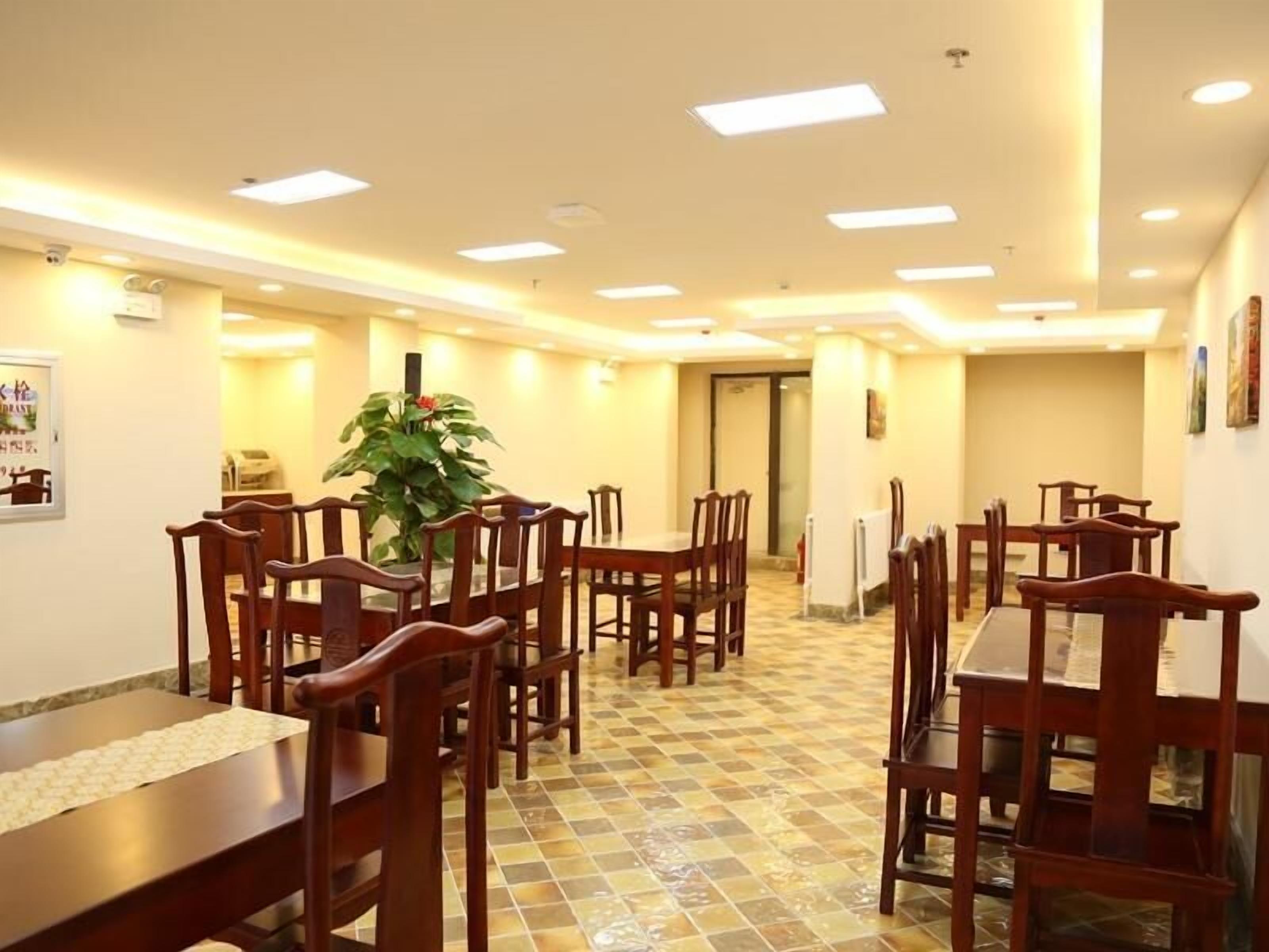 Un comedor con mesas y sillas de madera, una planta en maceta y piso de baldosas.