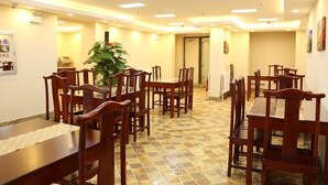 Un comedor con mesas y sillas de madera, una planta en maceta y piso de baldosas.