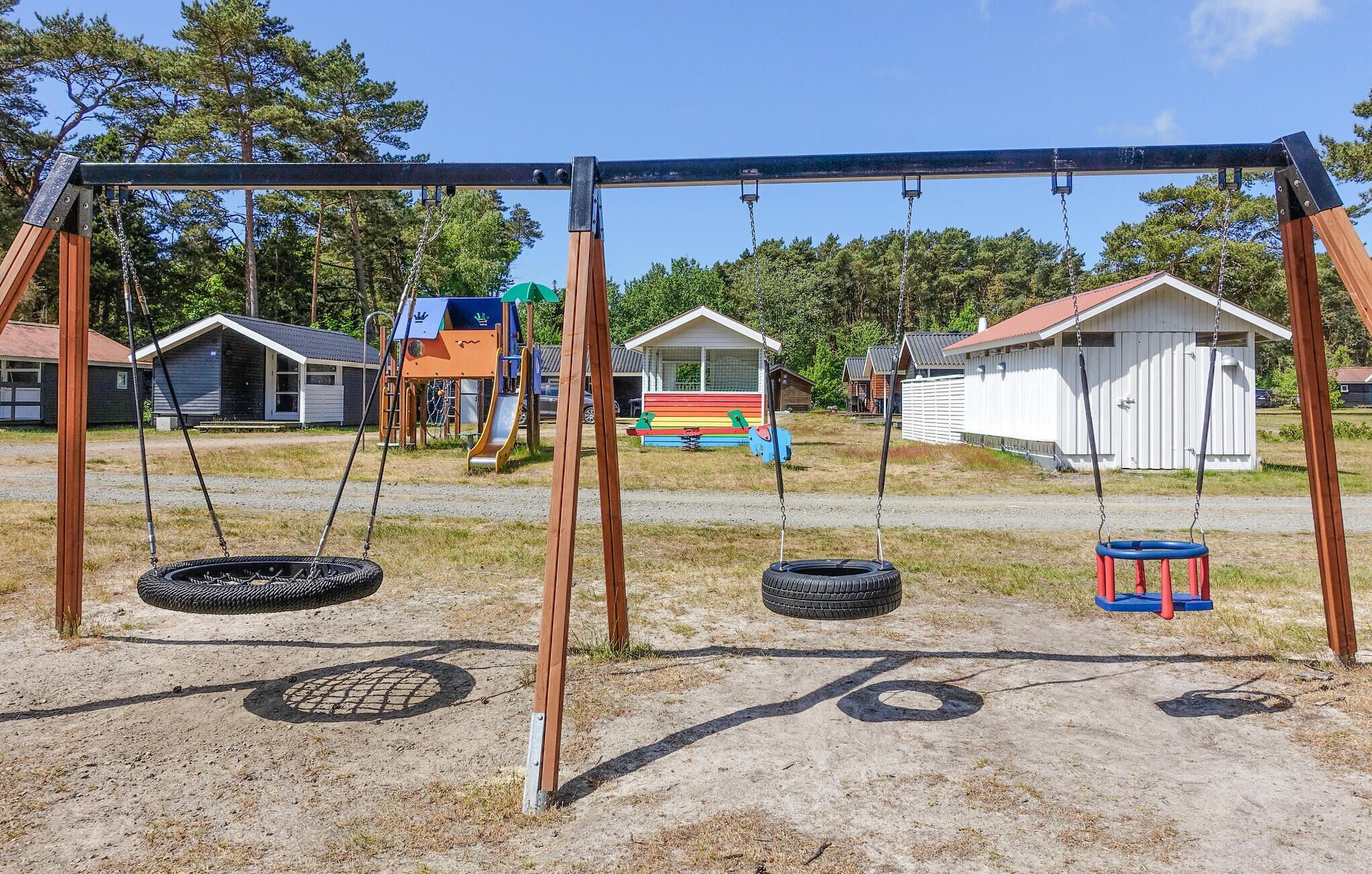 A playground with swings and tire swings, surrounded by small cabins and a grassy area.