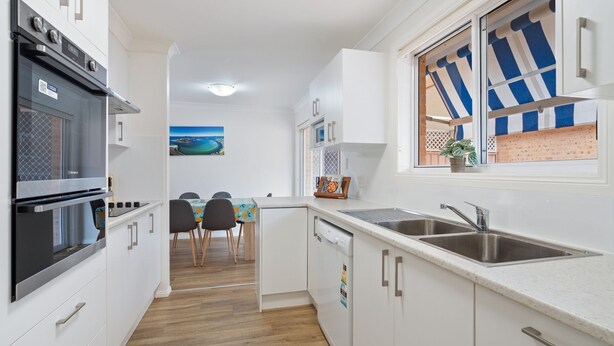A compact kitchen with a built-in oven, a sink, and a dining area with a view of the sea. - 4/27 South Street. Renovated three bedroom villa. (Tuncurry)