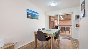 A dining area with a table, chairs, and a view through a glass door to an outdoor space. - 4/27 South Street. Renovated three bedroom villa. (Tuncurry)
