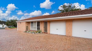 A two-story building with a brick facade, a garage with two white doors, and a paved driveway. - 4/27 South Street. Renovated three bedroom villa. (Tuncurry)