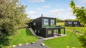 Una casa moderna negra con ventanas grandes, un balcón y un césped cuidado.