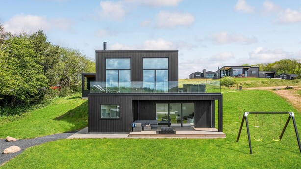 Una casa moderna de dos pisos con un balcón de cristal, rodeada de abundante vegetación.