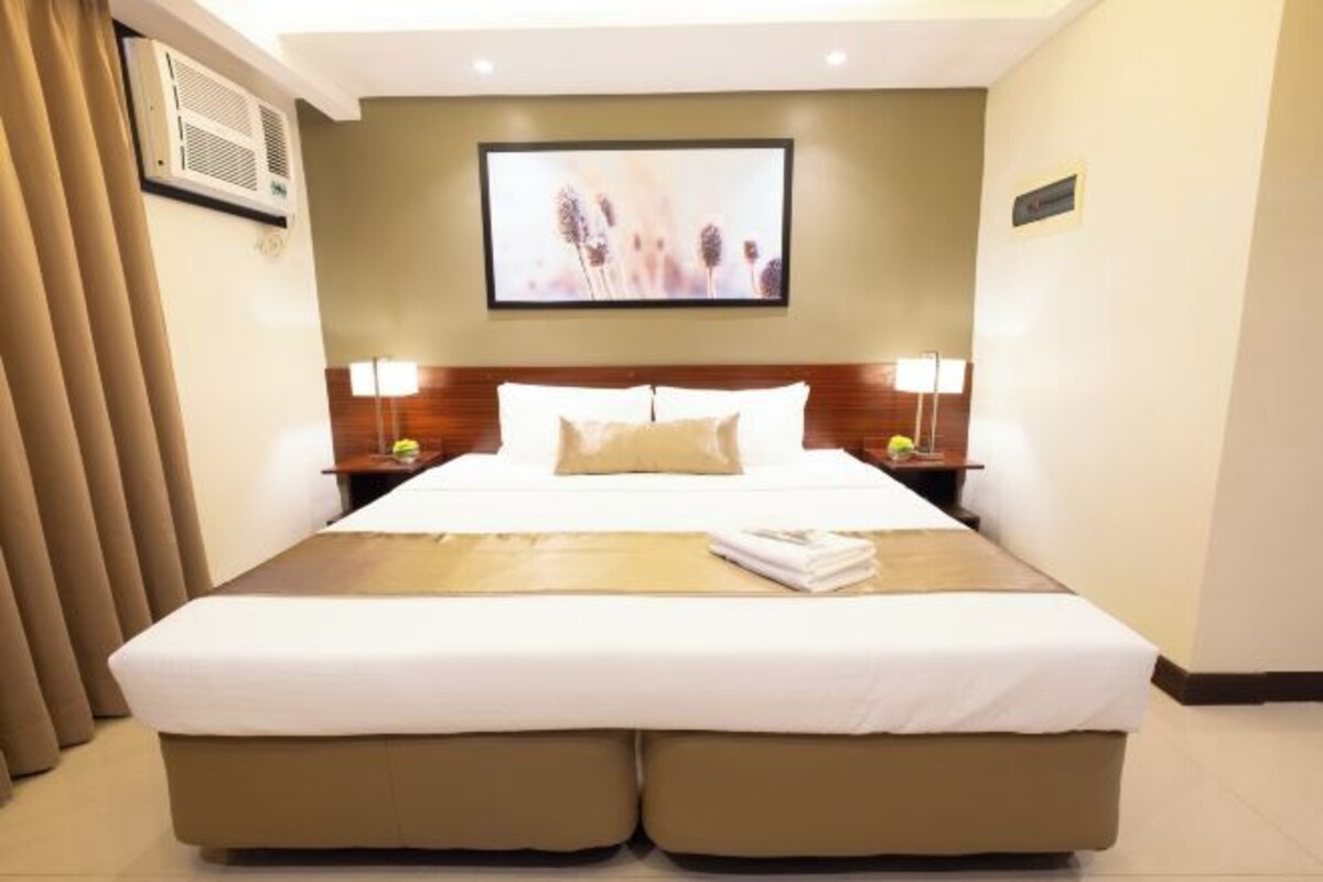 A hotel room with a large bed, two bedside tables, a wall-mounted TV, and a window with curtains.