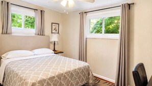 Ein Hotelzimmer mit einem Bett, einem Deckenventilator, einem Nachttisch mit Lampe und Blick auf Grünflächen.