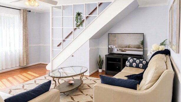 Ein Wohnzimmer mit einer Couch, einem Glastisch, einem Fernseher und einer Treppe.