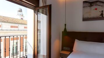 A hotel room with a large window, a bed, a nightstand, and a green pendant light.