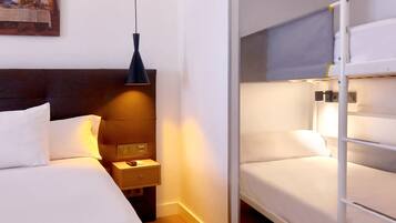 A hotel room with a single bed, a nightstand, a bedside table, a lamp, and a bunk bed.