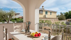 A balcony with a table set for two, featuring wicker chairs and a plate of fruit.