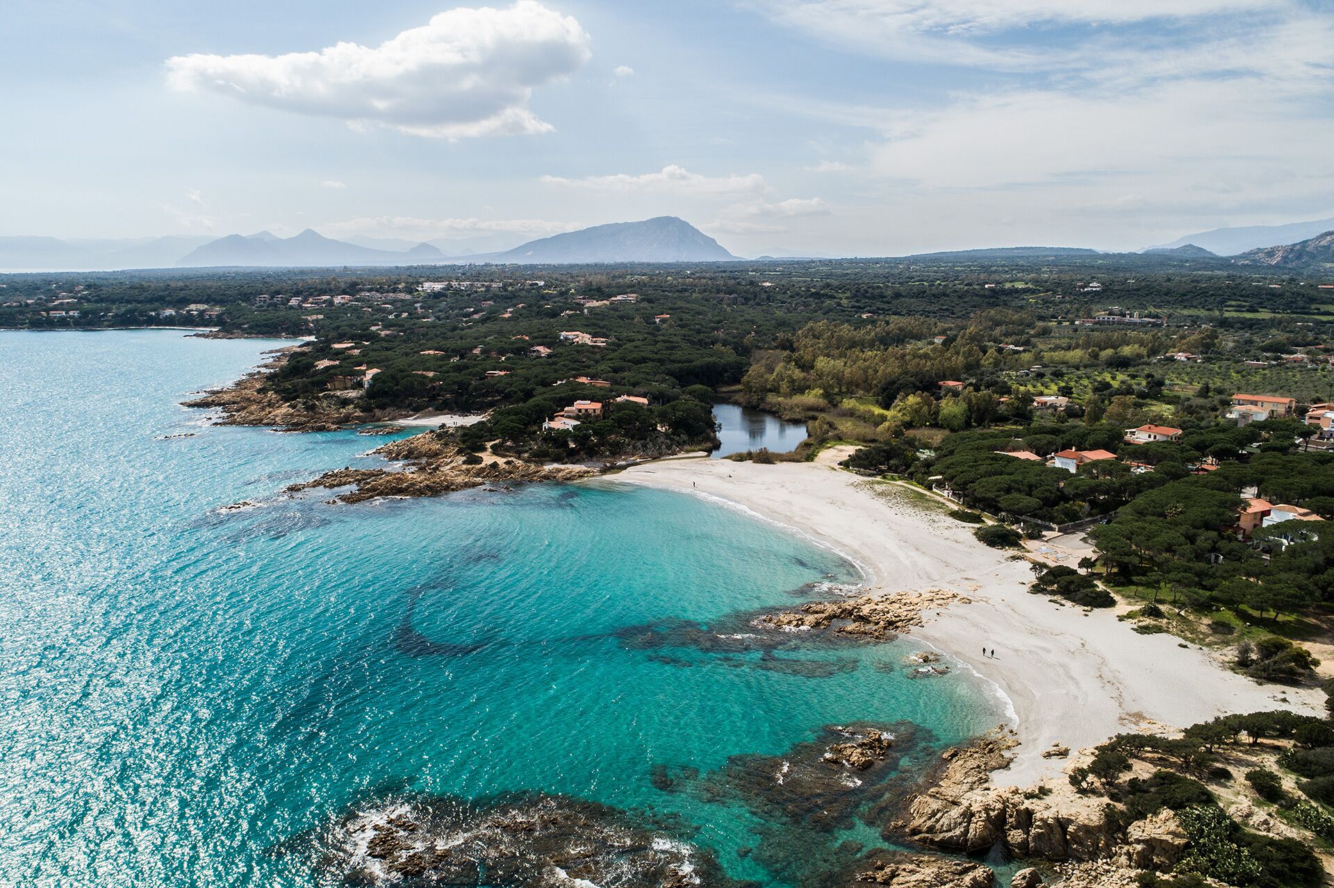 Une zone côtière dotée d’une plage, d’eaux turquoise et limpides, et d’un paysage montagneux en arrière-plan.