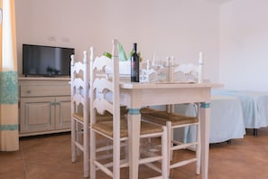 A dining area with a table set for two, a bottle of wine, and a glass. There is a television on a cabinet in the background.