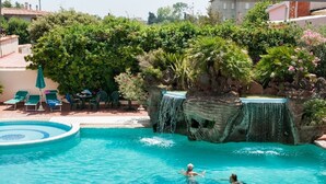 A swimming pool with a waterfall feature, surrounded by lush greenery and lounge chairs.