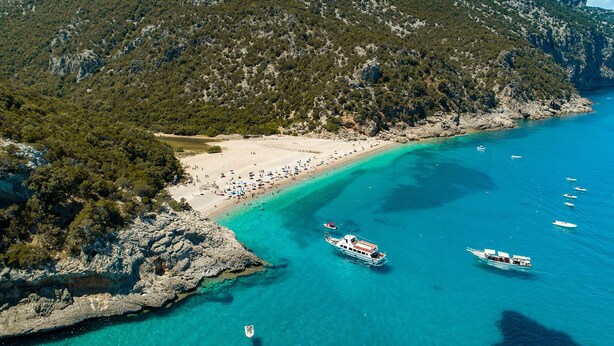 An aerial view of a coastal area with a beach, boats, and rocky terrain.
