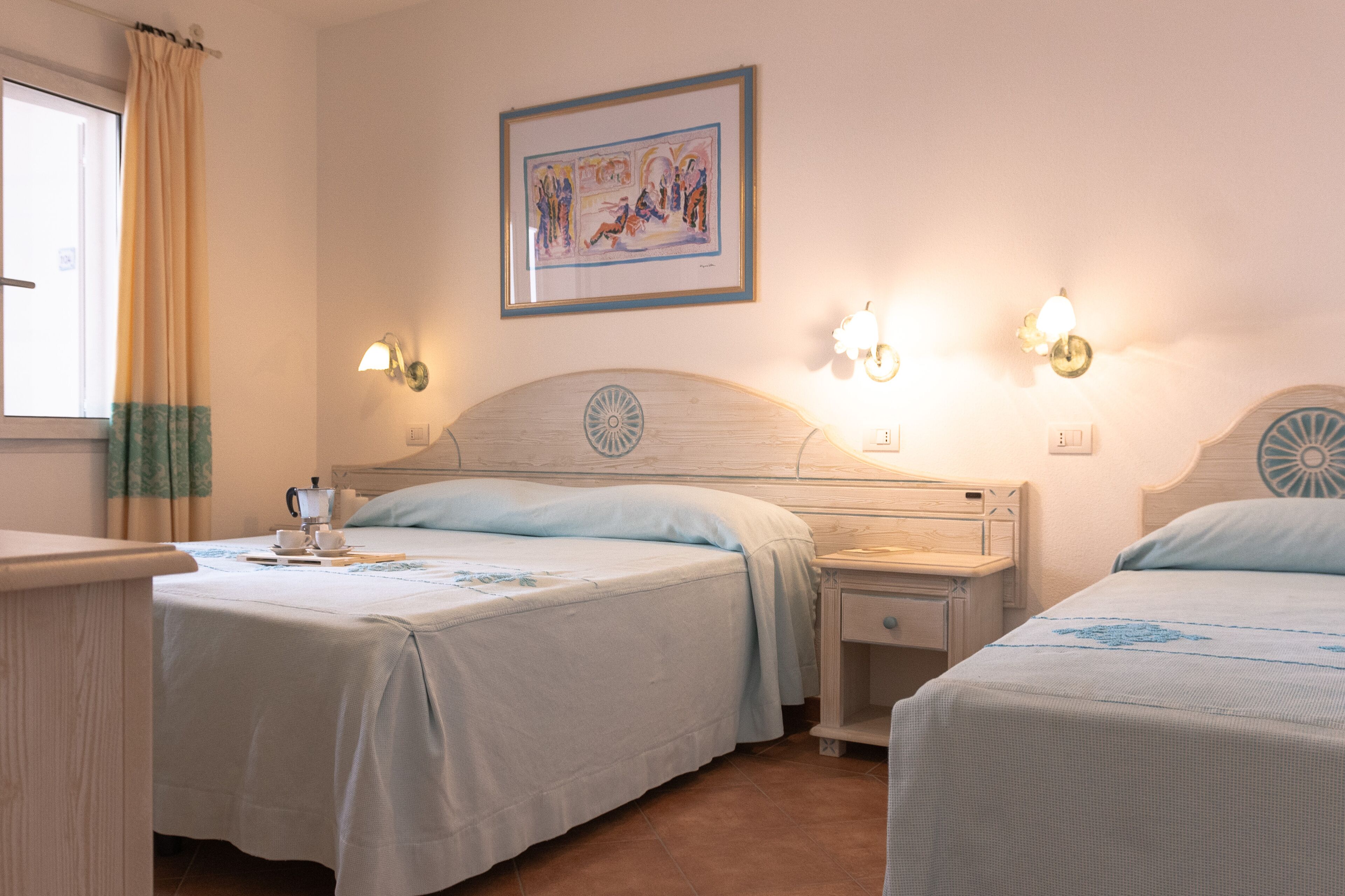 Une chambre d’hôtel avec deux lits, une table de chevet avec une lampe, un tableau encadré au mur et une fenêtre avec des rideaux.