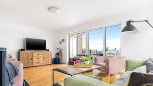 Ein modernes Wohnzimmer mit Flachbildfernseher, Holzschrank und großem Fenster mit Blick auf die Stadt.