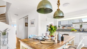Eine moderne Küche mit weißen Schränken, einem Holztisch und hängenden Pendelleuchten.