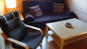 Una habitación acogedora con un sofá azul oscuro, dos almohadas estampadas, una mesa de madera y una silla.