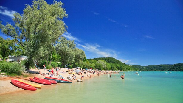 Una playa con kayaks alineados en la orilla, gente tomando el sol y un cielo azul despejado.