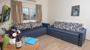 Una sala de estar moderna con un sofá azul, una mesa de centro de madera con una botella de vino y copas, un jarrón de flores y una carpeta azul.