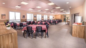 Un comedor amplio con varias mesas y sillas, ventanas grandes y una encimera de madera con un jarrón de flores.