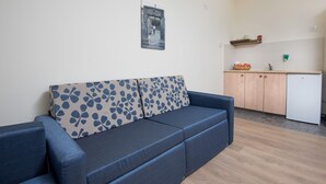 Una sala de estar con sofá, un área de cocina con alacenas y refrigerador, y un cuadro colgado en la pared.