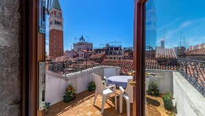 A balcony with a table and chairs, potted plants, and a view of historic buildings and a tower. - Hotel ai do Mori (Venice)