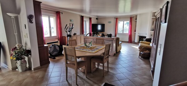 A spacious living area with a dining table, chairs, a sofa, a TV, and exercise equipment.