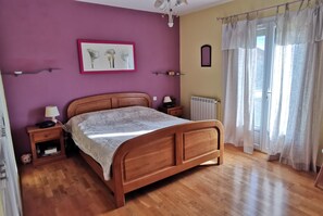A bedroom with a wooden bed, a nightstand with a lamp, a radiator, and a window with curtains.