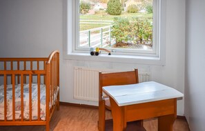 A room with a wooden crib, a small wooden table, and a window with a view of a garden and houses. - Lovely home in Tranås with sauna (Tranås)
