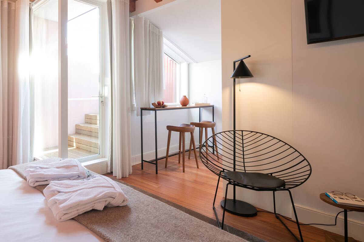 Una habitación de hotel moderna con cama, escritorio, silla y un ventanal grande.