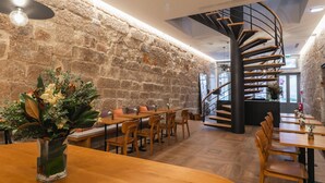 A restaurant with wooden tables and chairs, a stone wall, and a spiral staircase. - Porto River Infante (Porto)