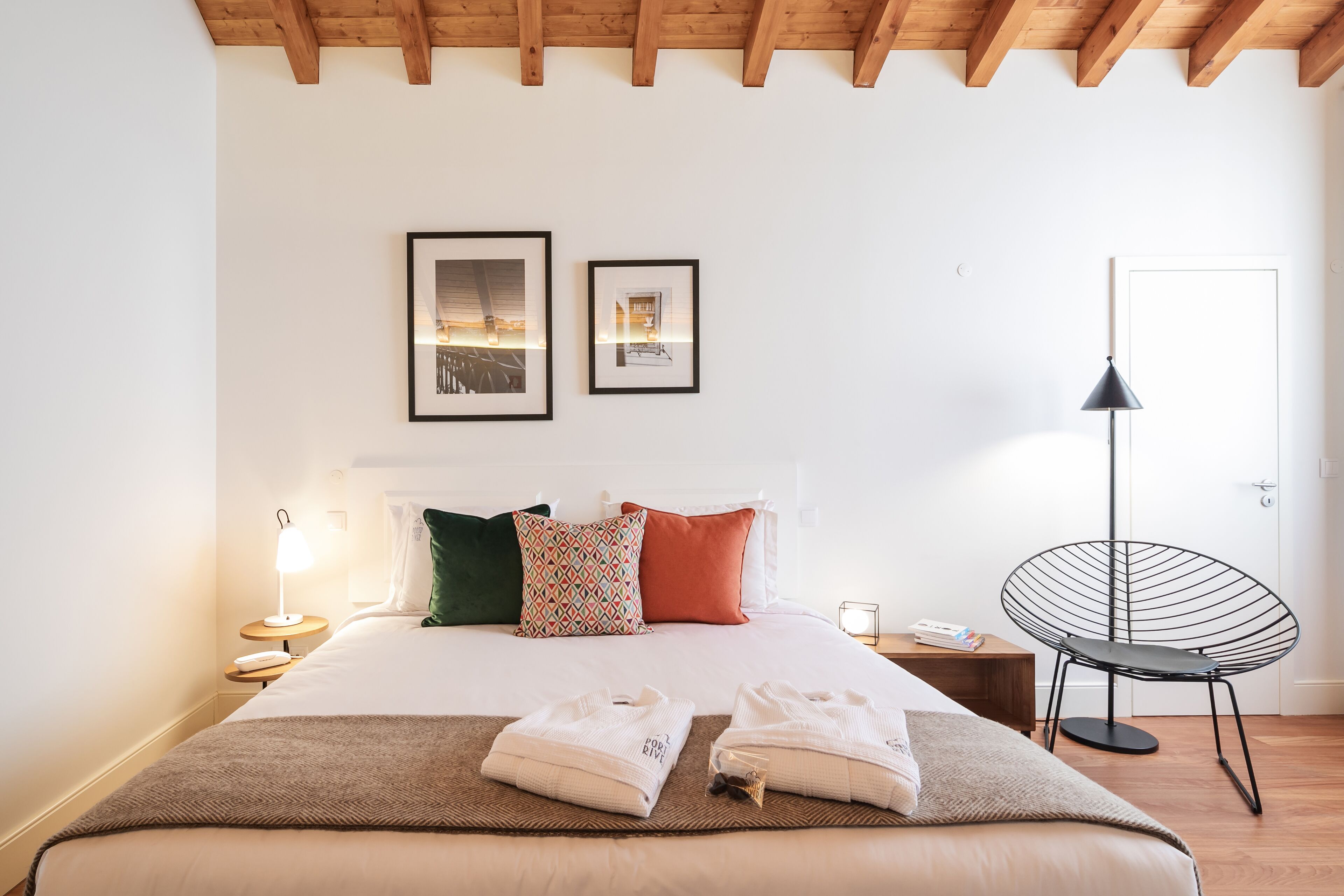 A neatly made bed with a patterned pillow, a black chair, and a bedside table with a lamp.