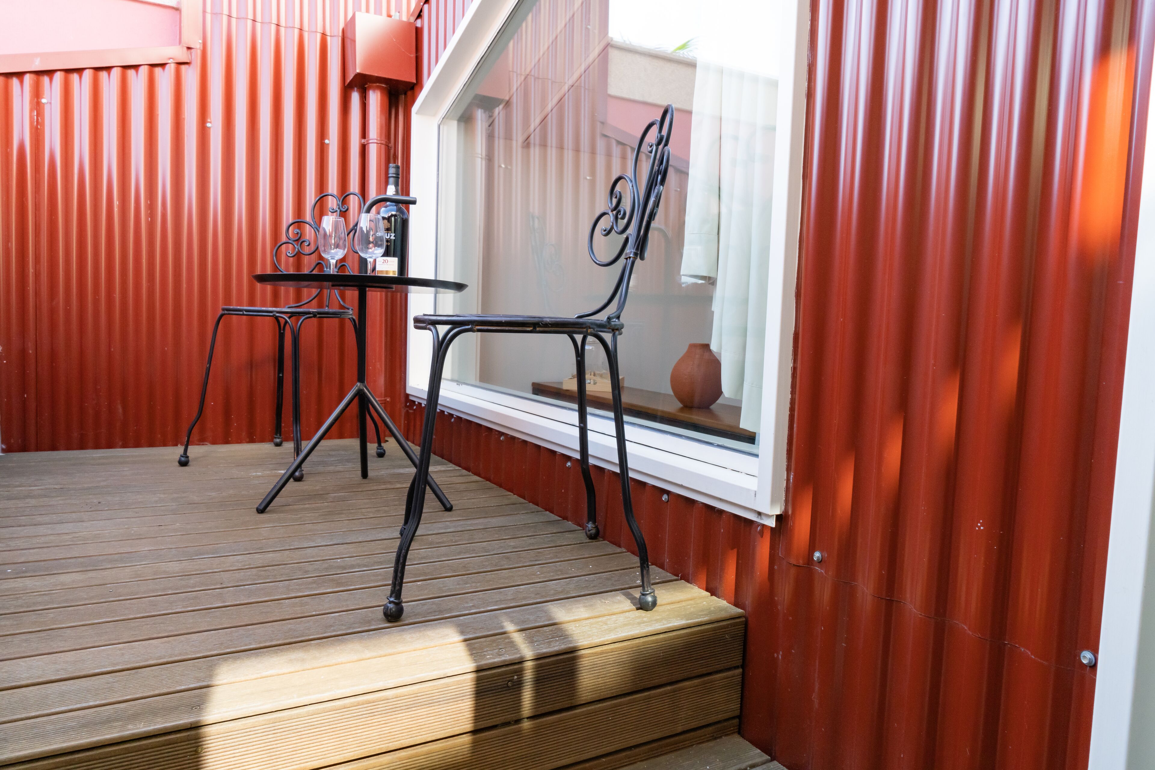 A wooden deck with a table and chairs, a window with a view, and a red wall.
