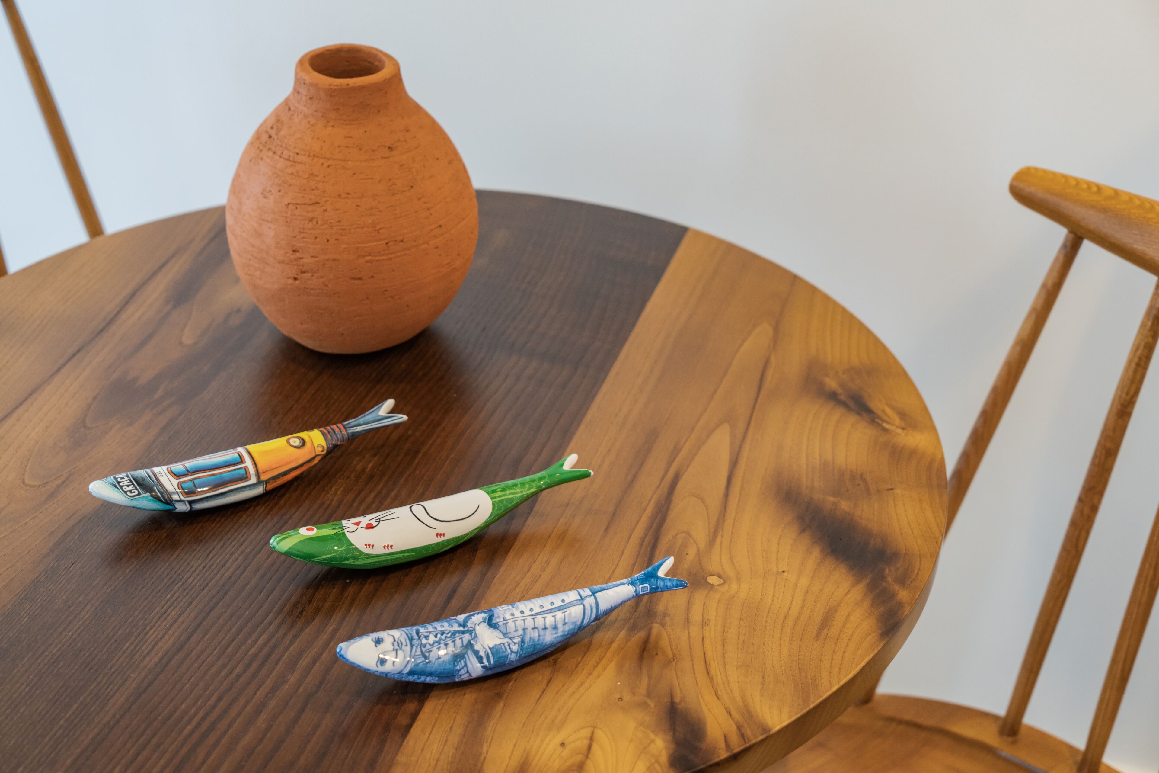 A round wooden table with a clay pot and three ceramic fish.