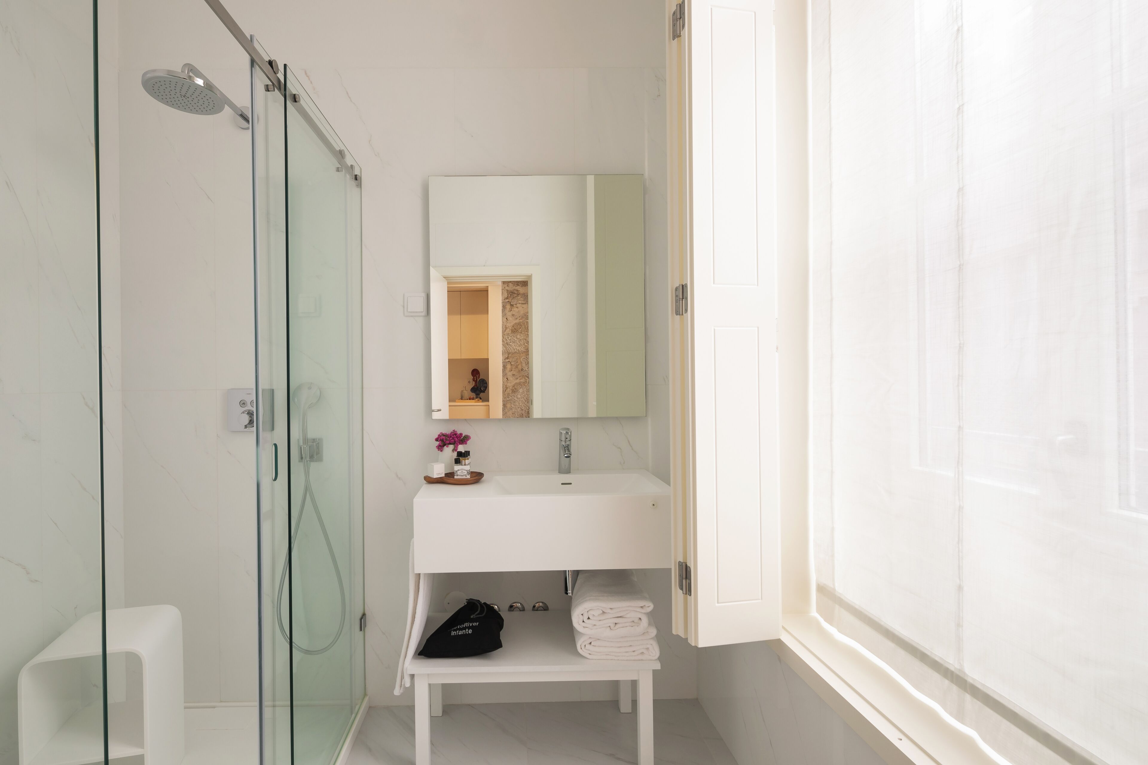 A modern bathroom with a glass shower enclosure, a white sink with a mirror above, and a small shelf with towels and toiletries.