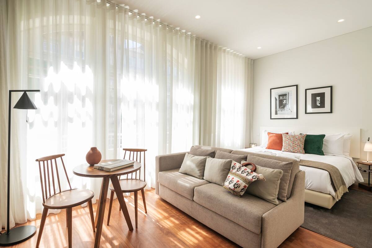 Una habitación de hotel moderna con sofá, una pequeña mesa de comedor y una cama.