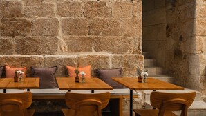 A stone wall with a bench and tables, wooden chairs, and a small vase with flowers. - Porto River Infante (Porto)