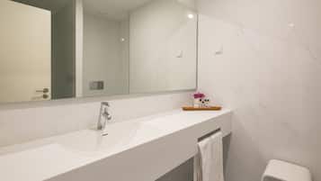 Un baño moderno con un lavamanos de mármol blanco, un espejo grande y un taburete blanco pequeño.