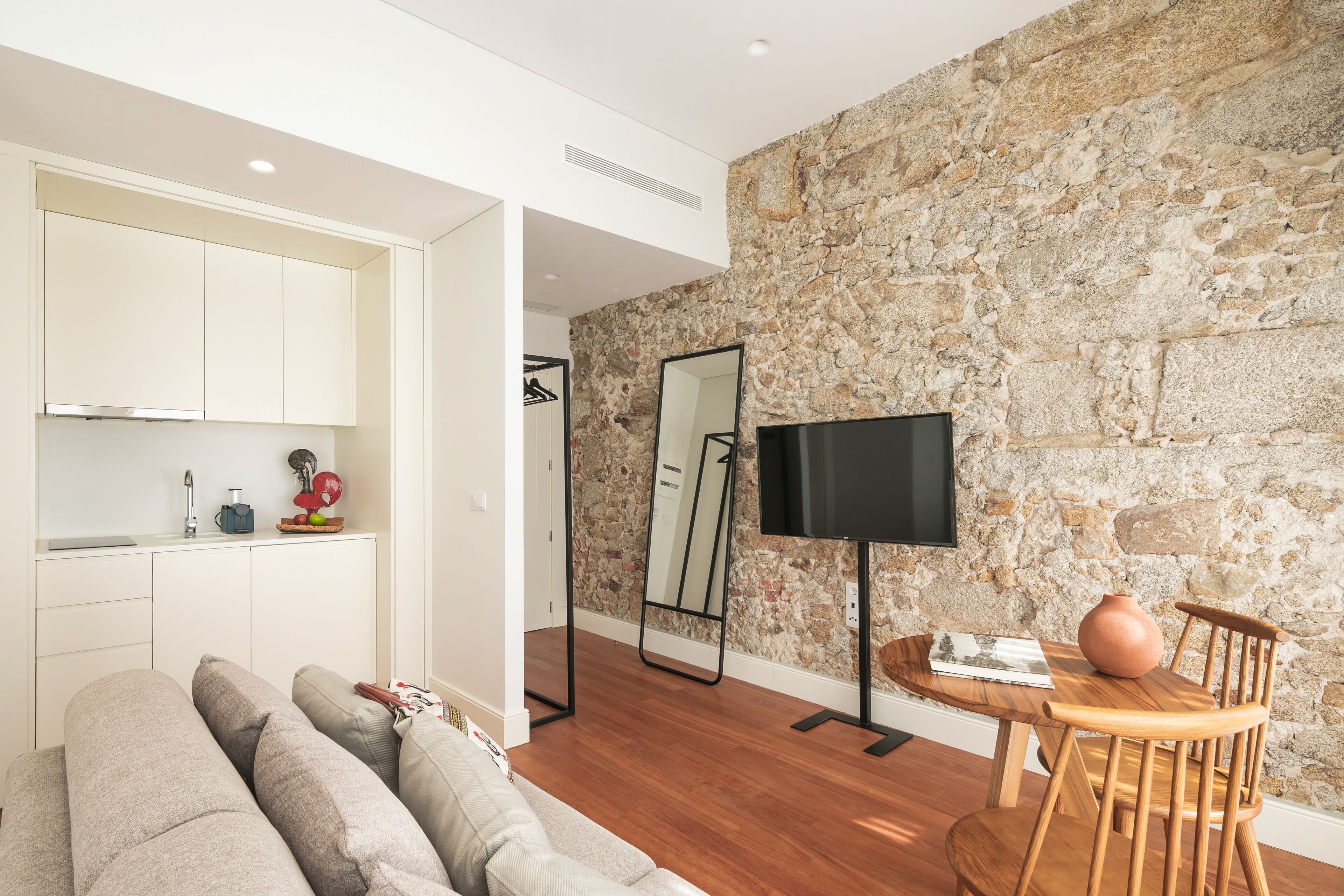A modern living room with a stone wall, a flat-screen TV, a wooden dining table, and a sofa.