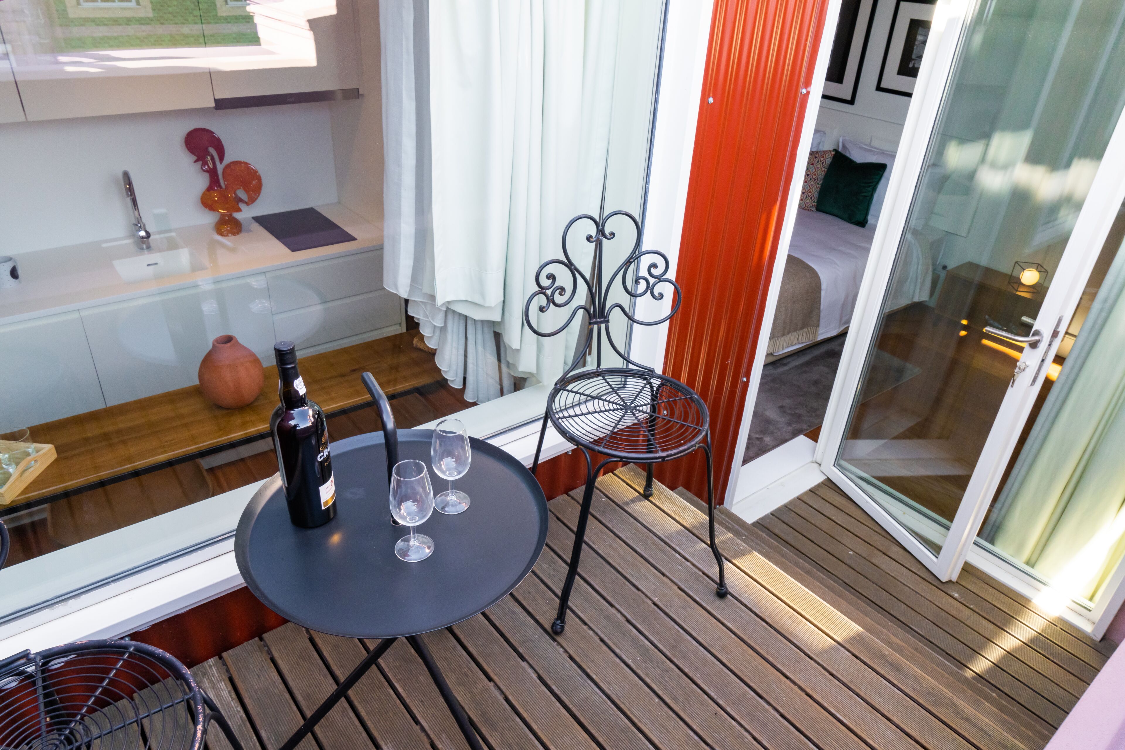 A balcony with a table, a chair, a bottle of wine, and a vase.