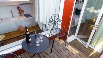 A balcony with a table, a chair, a bottle of wine, and a vase.