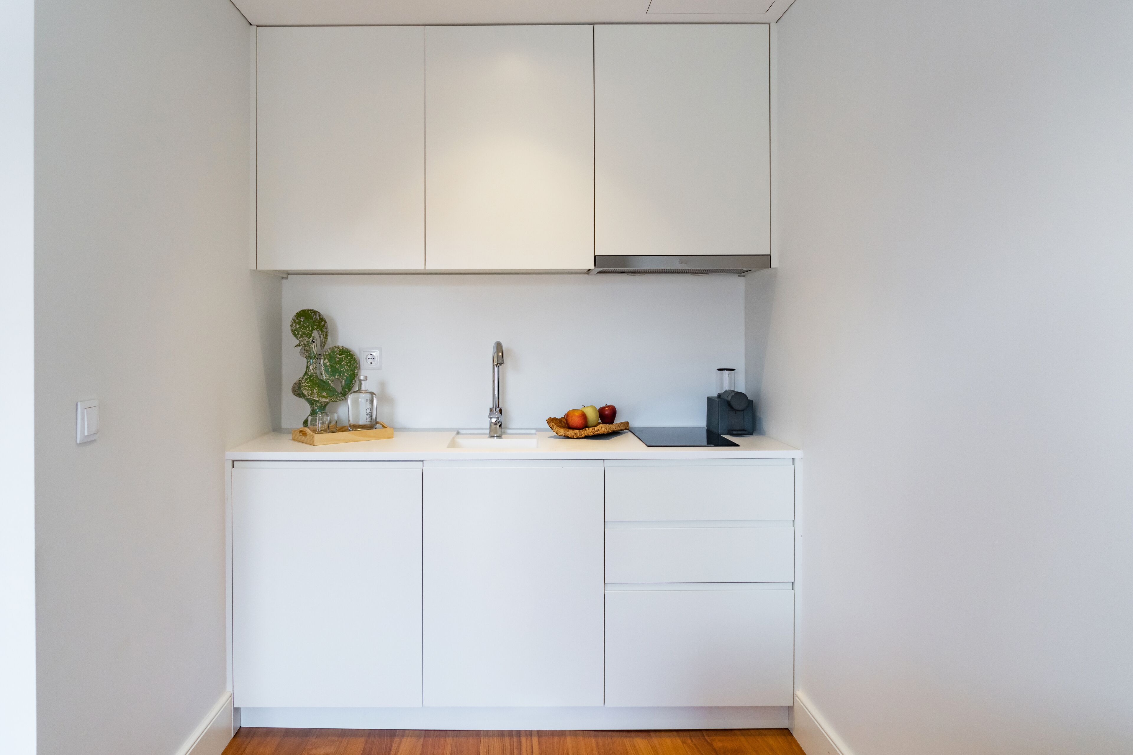 A compact kitchen with white cabinets, a sink, and a countertop with a fruit bowl and a plant.