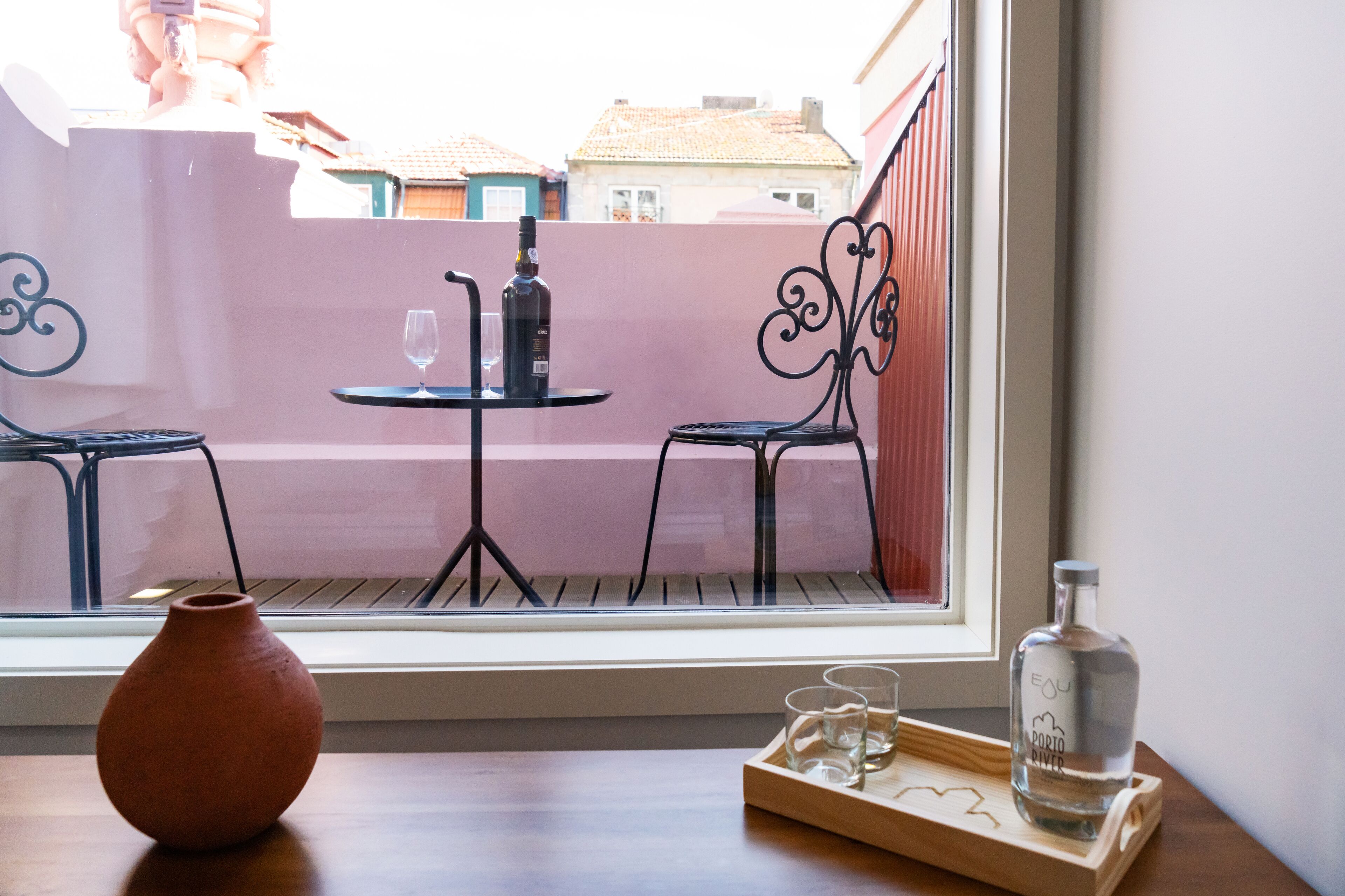 Een balkon met een tafel, stoelen, een vaas en een fles op een dienblad.