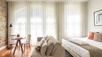 Una habitación de hotel moderna con una cama grande, un sofá, una mesa de comedor con sillas y una pared de piedra.