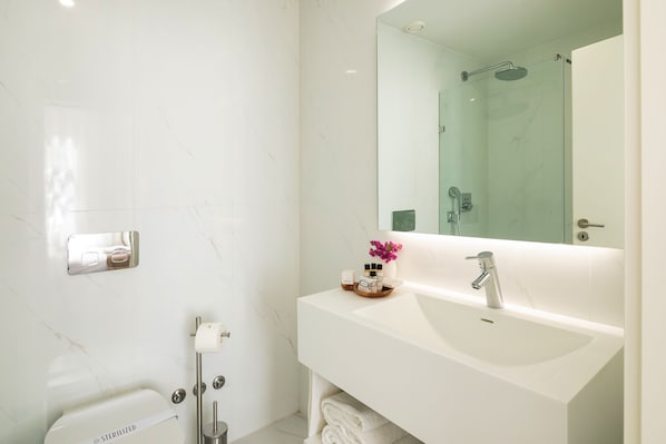 Un baño moderno con un lavabo blanco, un espejo grande y una zona de ducha.