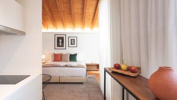 A bedroom with a bed, bedside table, and a nightstand. There is a window with curtains and a view of the outside.