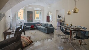A spacious living area with a modern sofa, a dining table with chairs, and a kitchen in the background.
