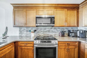 A kitchen with wooden cabinets, a stainless steel microwave, a gas stove, and a coffee maker.